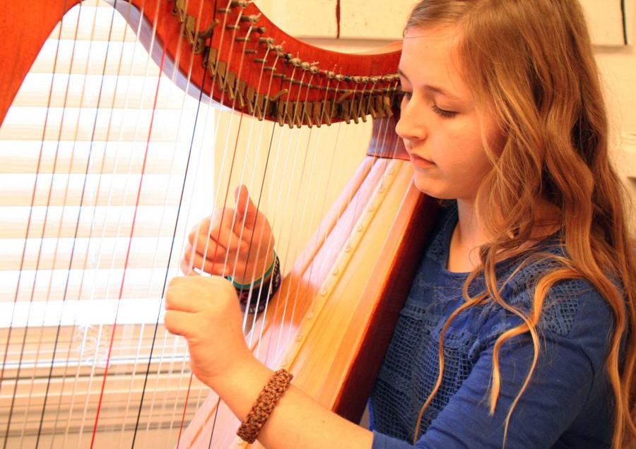 In her room, freshman Emily Mellor plays one of her two harps.