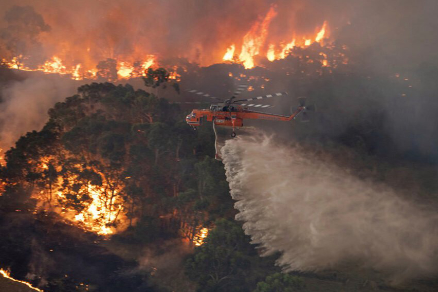 In this Monday, Dec. 30, 2019 photo provided by State Government of Victoria, a helicopter tackles a wildfire in East Gippsland, Victoria state, Australia. Wildfires burning across Australias two most-populous states trapped residents of a seaside town in apocalyptic conditions Tuesday, Dec. 31, and were feared to have destroyed many properties and caused fatalities. (State Government of Victoria via AP)