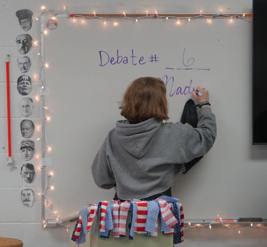 Junior Mikayla Arbeene writes the name of the fourth U.S. president, James Madiso, on a whiteboard before her debate begins. 