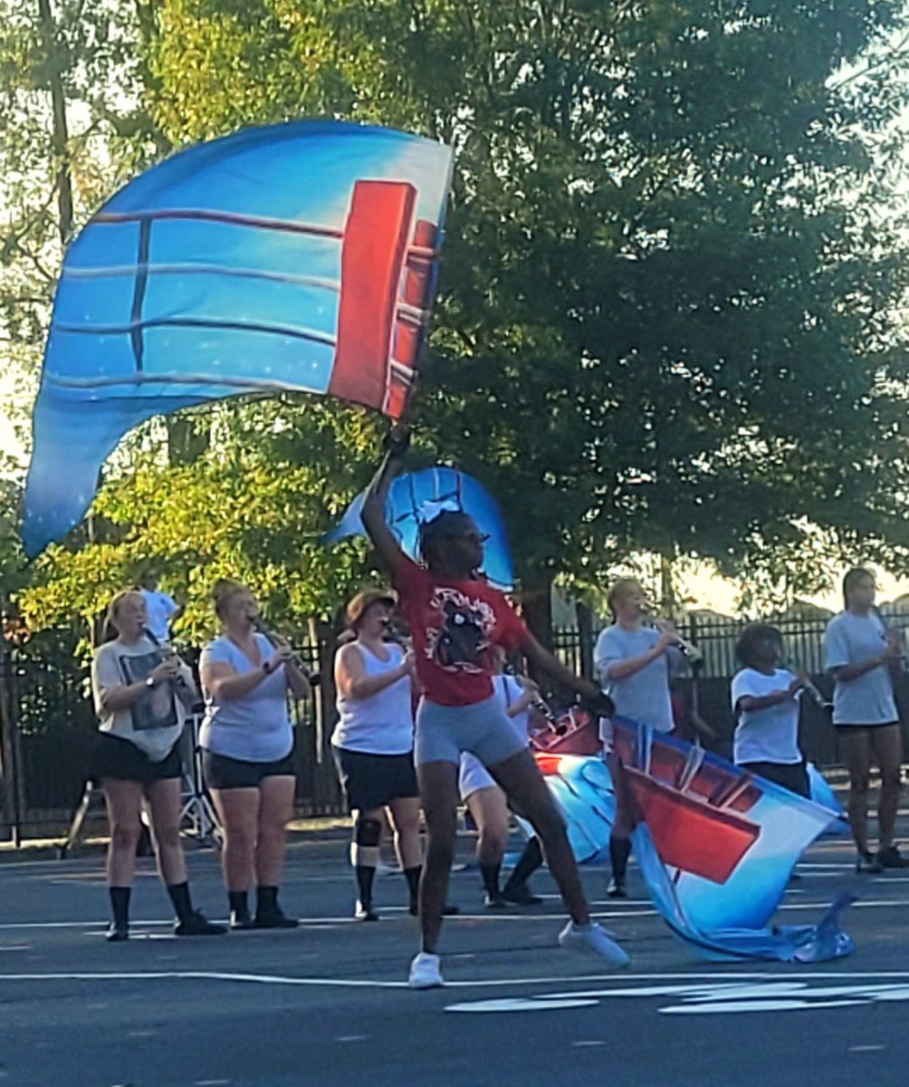 Color Guard member practicing choreo as the Legacy of Bryant band plays in the background. 