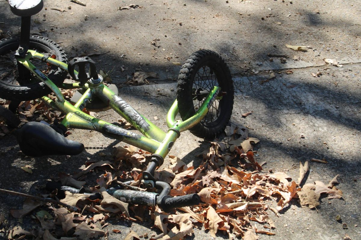 A broken tricycle lays on a driveway.