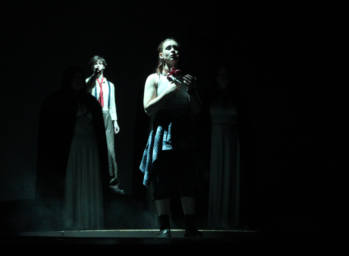 Obscured by the Fates, sophomore Carter Sullivan, playing Orpheus, reaches out for senior Liv Robertson, portraying Eurydice, as clutches the flower he created to her chest.