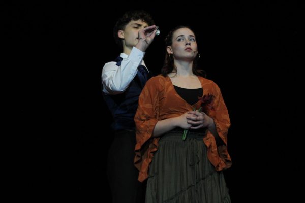 Junior Braden Lisowe, playing Hades, presents senior Liv Robertson, portraying Eurydice, with a chance to escape poverty, offering her the train fare to Hadestown.
