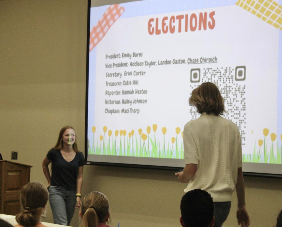 Reporter Addison Taylor steps away from the podium after announcing the beginning of officer elections during the final Beta Club Meeting of the 2024-2025 school year in the MPR. Chaplain Landon Gaston takes the floor to introduce the candidates.