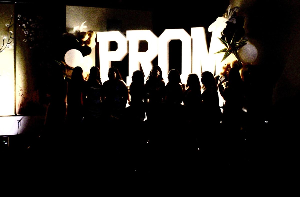 Attendees of the 2025 Great Gatsby Prom pose for a group photo in front of the “Prom” sign in the ballroom of the Benton Event Center.
